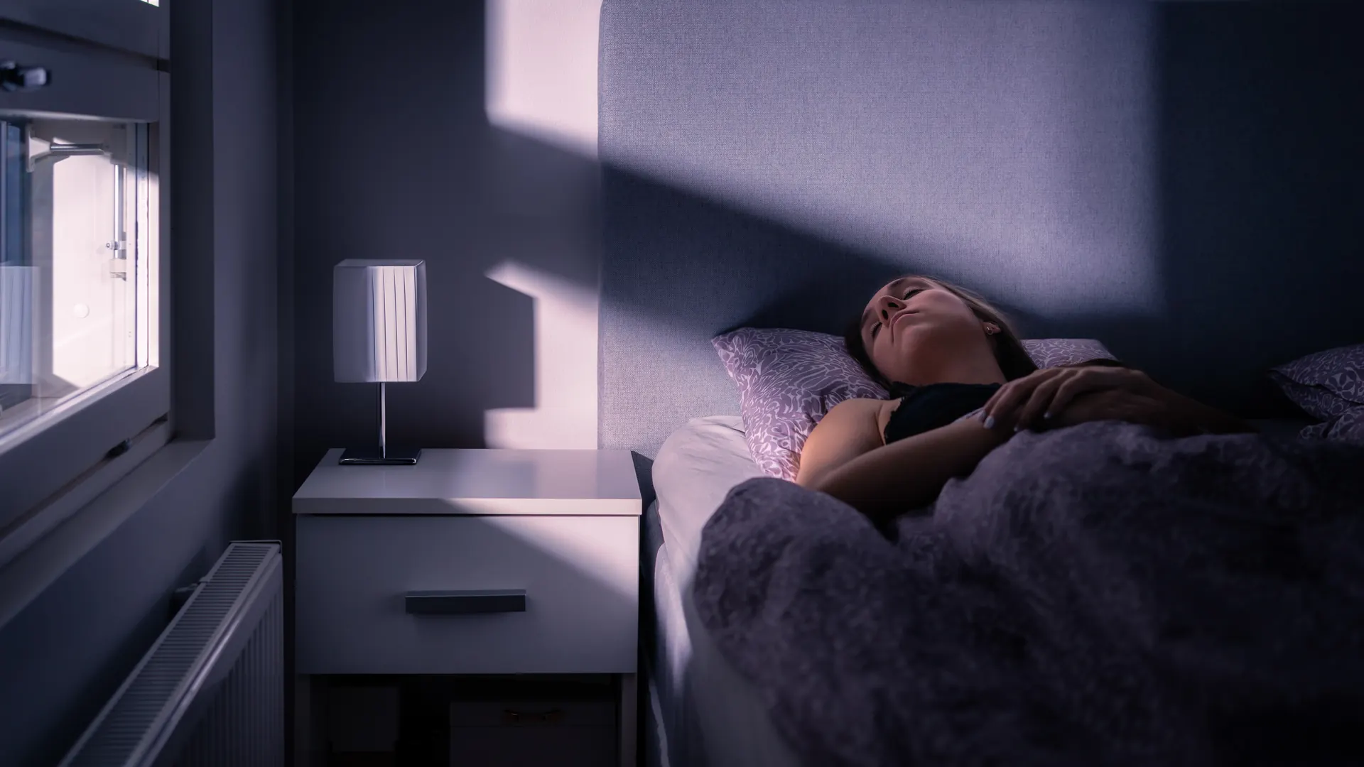 A woman asleep in a dark bedroom with a soft beam of light across the bed